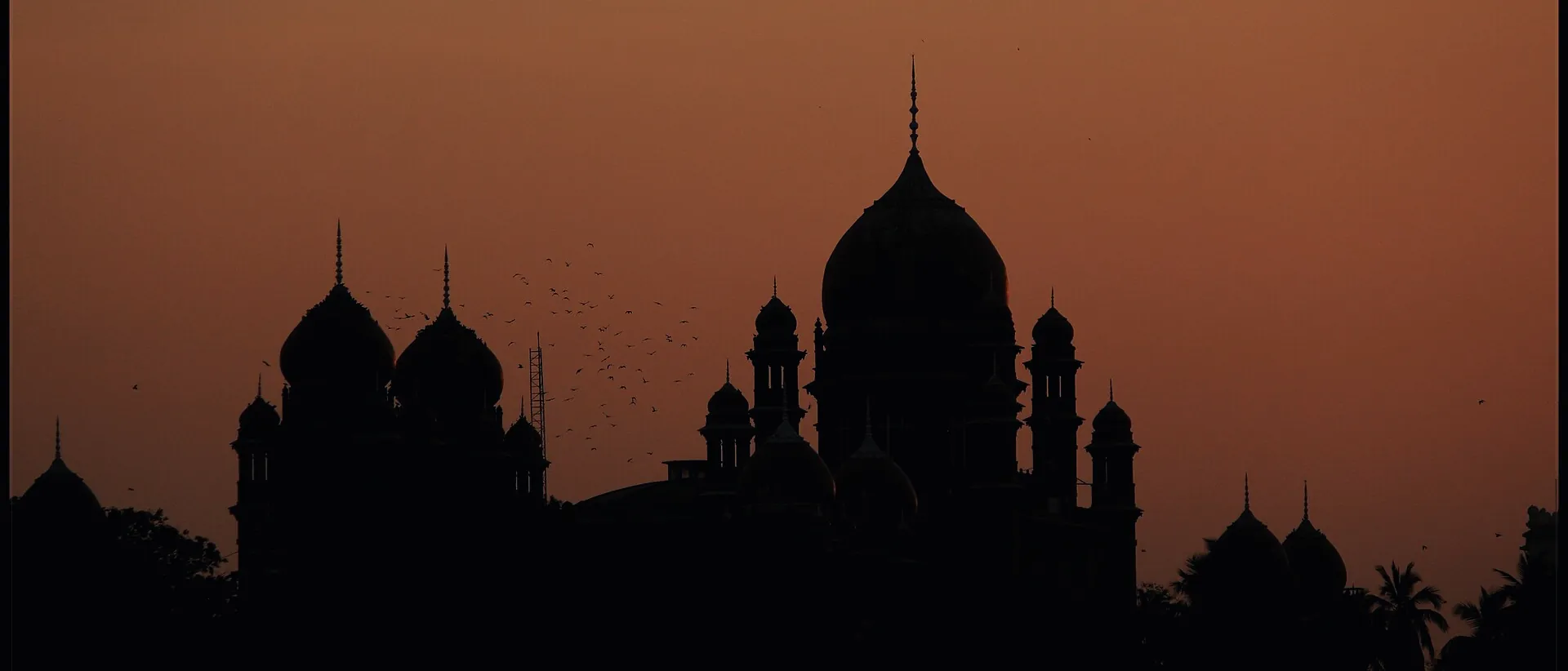 The domes of the Telangana High Court in Hyderabad silhouetted against a sunset